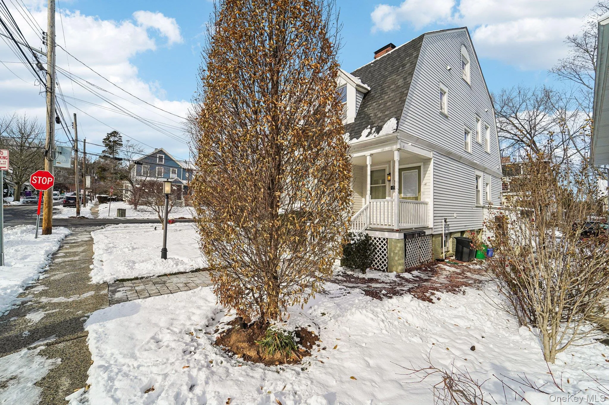 Snow covered property with a gambrel roof, covered porch, a shingled roof, and a chimney Snow covered property with a gambrel roof, covered porch, a shingled roof, and a chimney