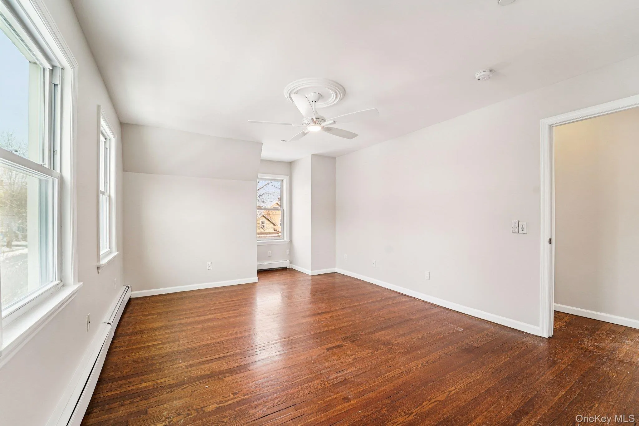 Unfurnished room with a baseboard radiator, dark wood-type flooring, and a ceiling fan Unfurnished room with a baseboard radiator, dark wood-type flooring, and a ceiling fan