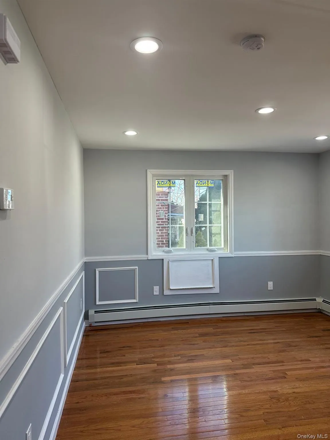 Empty room featuring wainscoting, a baseboard heating unit, a decorative wall, dark wood-type flooring, and recessed lighting Empty room featuring wainscoting, a baseboard heating unit, a decorative wall, dark wood-type flooring, and recessed lighting