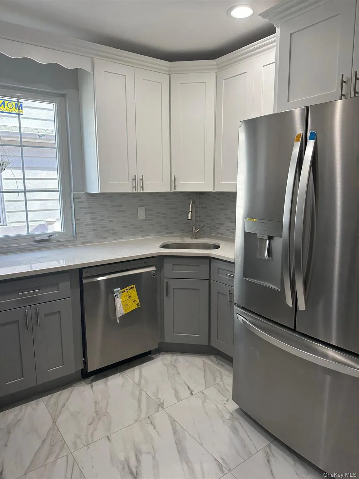 Kitchen with appliances with stainless steel finishes, gray cabinets, light marble finish floors, light stone counters, and white cabinetry Kitchen with appliances with stainless steel finishes, gray cabinets, light marble finish floors, light stone counters, and white cabinetry
