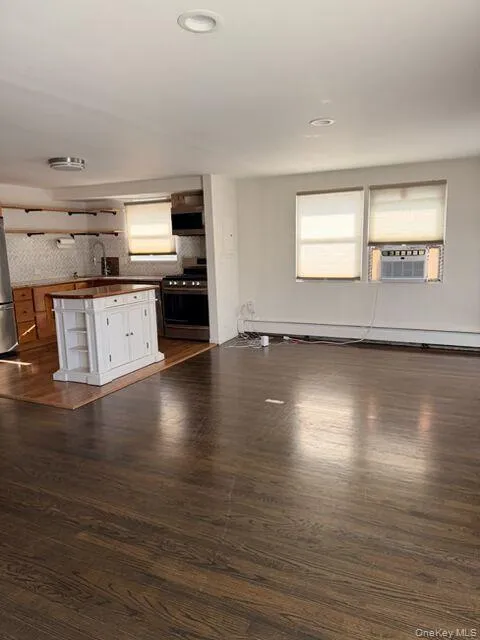 Unfurnished living room featuring plenty of natural light, dark wood-style floors, a baseboard heating unit, and cooling unit Unfurnished living room featuring plenty of natural light, dark wood-style floors, a baseboard heating unit, and cooling unit