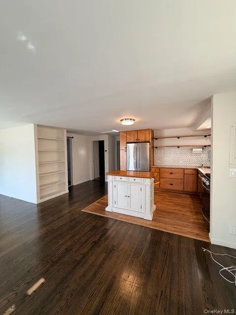 Kitchen featuring open floor plan, a center island, freestanding refrigerator, dark wood finished floors, and brown cabinets Kitchen featuring open floor plan, a center island, freestanding refrigerator, dark wood finished floors, and brown cabinets