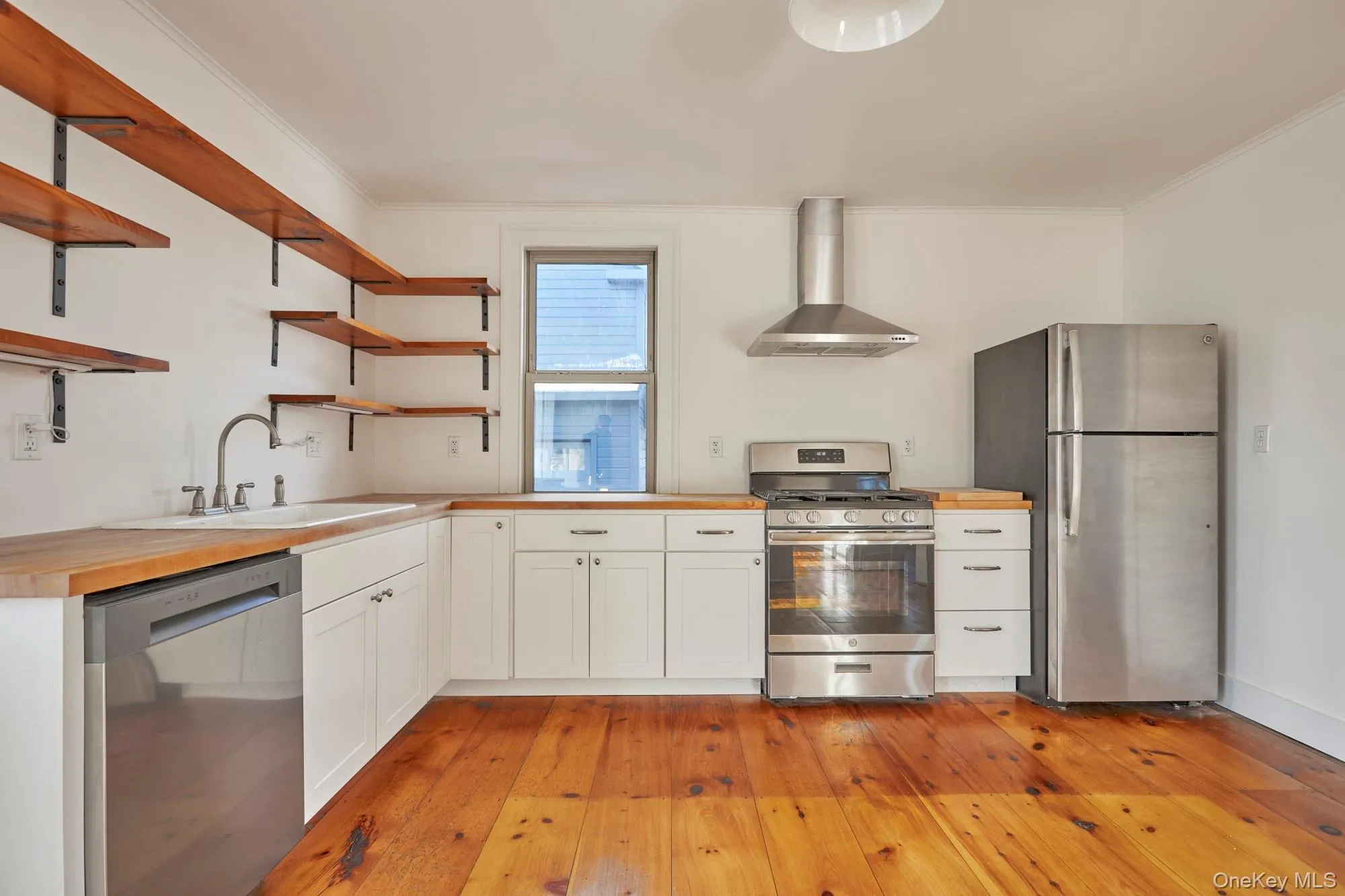 Kitchen with butcher block counters, white cabinetry, stainless steel appliances, wall chimney range hood, and light wood finished floors Kitchen with butcher block counters, white cabinetry, stainless steel appliances, wall chimney range hood, and light wood finished floors