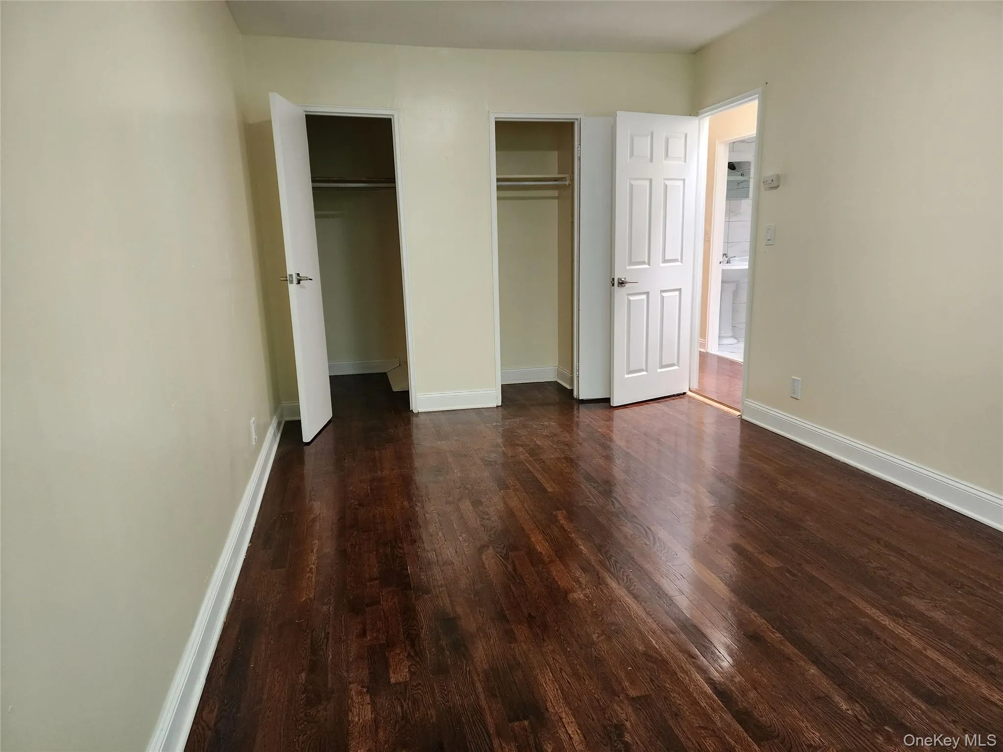 Unfurnished bedroom featuring multiple closets and dark wood-style flooring Unfurnished bedroom featuring multiple closets and dark wood-style flooring