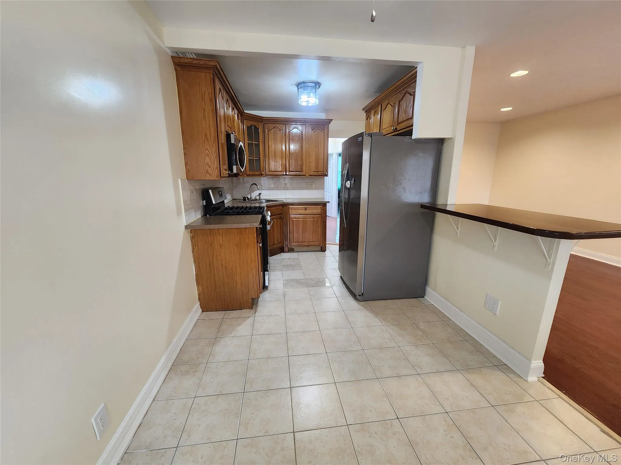 Kitchen featuring dark countertops, a kitchen bar, brown cabinets, and appliances with stainless steel finishes Kitchen featuring dark countertops, a kitchen bar, brown cabinets, and appliances with stainless steel finishes