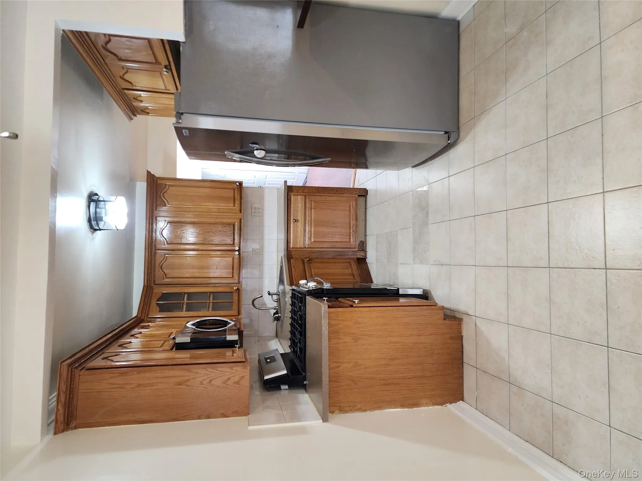 Kitchen with brown cabinetry, stainless steel appliances, decorative backsplash, glass insert cabinets, and light tile patterned floors Kitchen with brown cabinetry, stainless steel appliances, decorative backsplash, glass insert cabinets, and light tile patterned floors