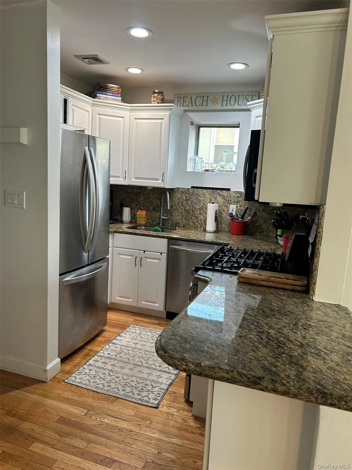 Kitchen featuring dark stone countertops, appliances with stainless steel finishes, white cabinetry, light wood-type flooring, and tasteful backsplash Kitchen featuring dark stone countertops, appliances with stainless steel finishes, white cabinetry, light wood-type flooring, and tasteful backsplash