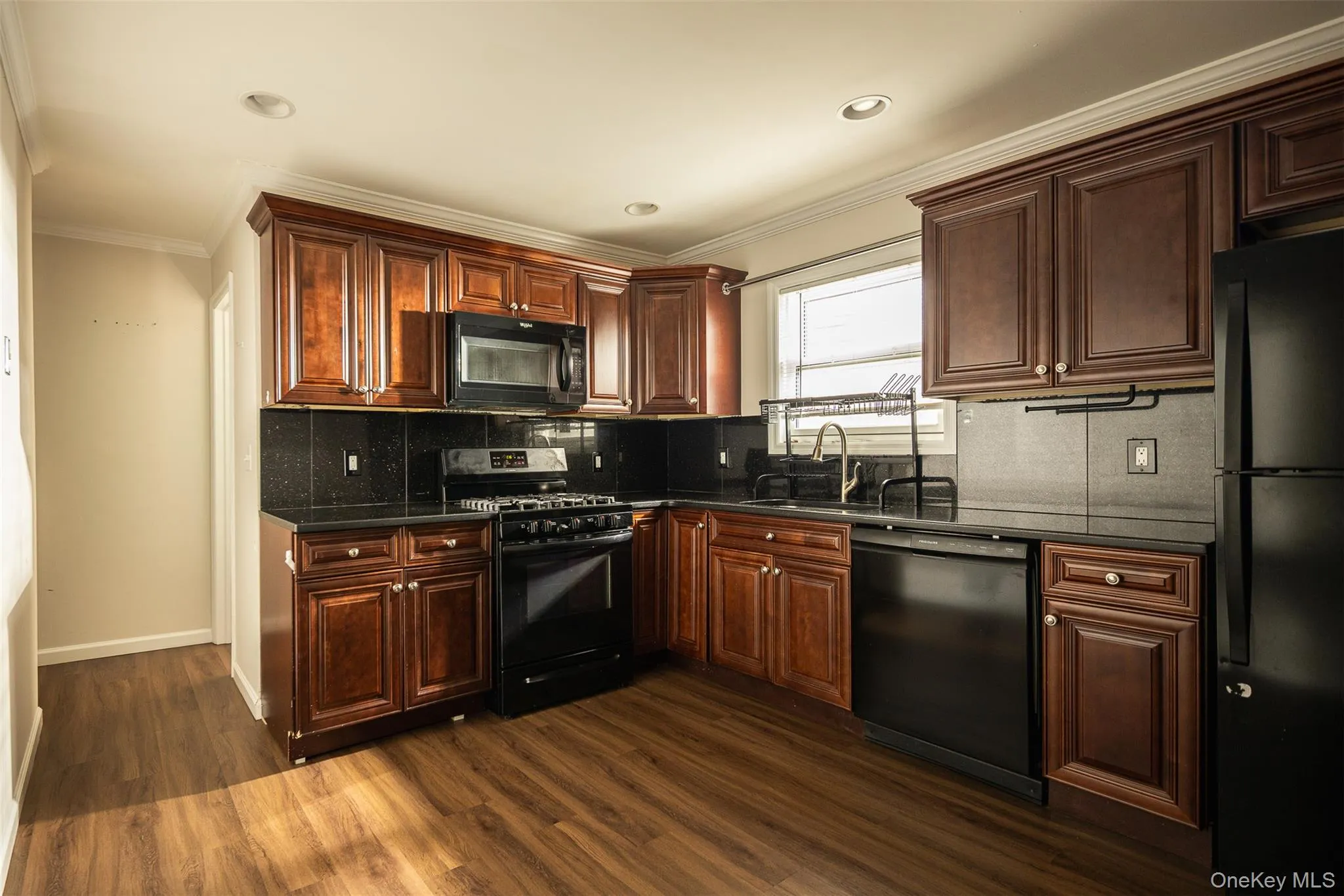Kitchen with black appliances, ornamental molding, dark wood finished floors, decorative backsplash, and dark stone countertops Kitchen with black appliances, ornamental molding, dark wood finished floors, decorative backsplash, and dark stone countertops