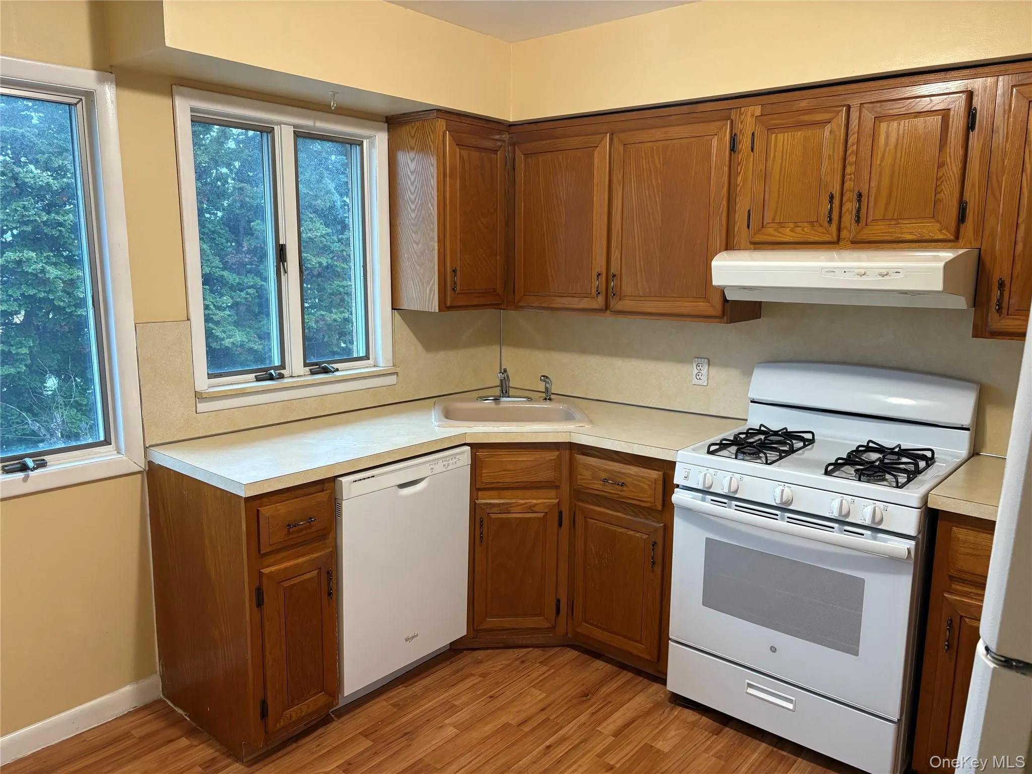 Kitchen with white appliances, brown cabinetry, light countertops, and range hood Kitchen with white appliances, brown cabinetry, light countertops, and range hood