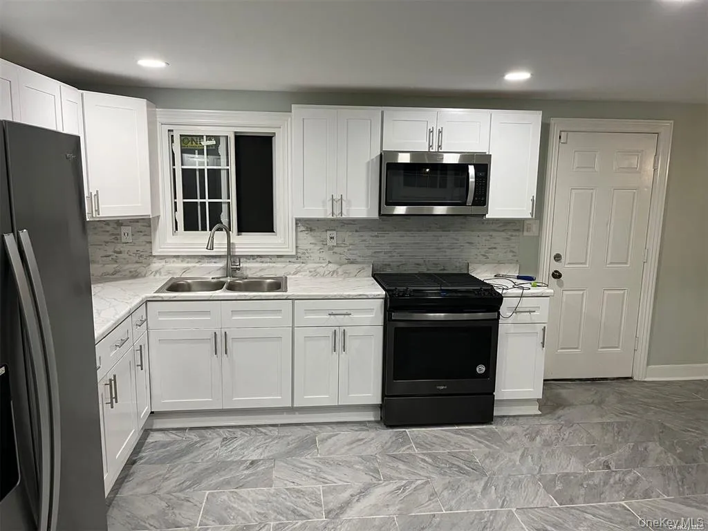 Kitchen featuring black appliances, light countertops, white cabinetry, backsplash, and light marble finish flooring Kitchen featuring black appliances, light countertops, white cabinetry, backsplash, and light marble finish flooring