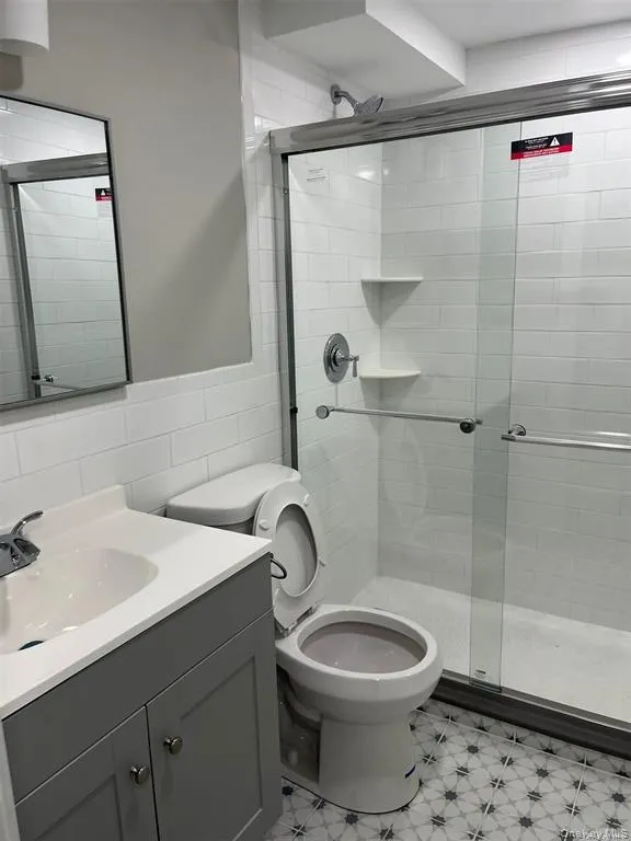 Bathroom with light flooring, a shower stall, tile walls, and vanity Bathroom with light flooring, a shower stall, tile walls, and vanity