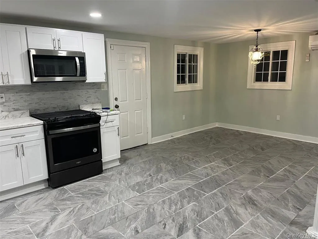 Kitchen with range with gas cooktop, stainless steel microwave, white cabinets, tasteful backsplash, and pendant lighting Kitchen with range with gas cooktop, stainless steel microwave, white cabinets, tasteful backsplash, and pendant lighting
