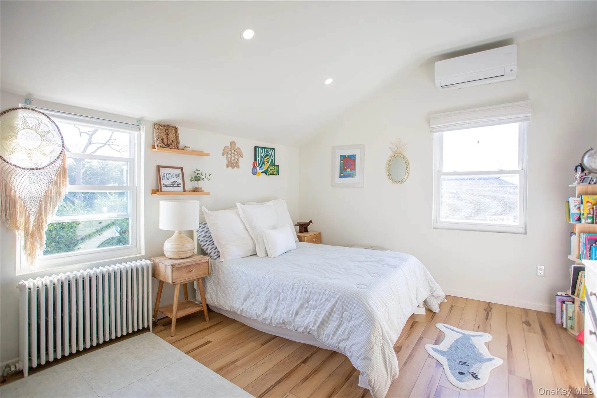 Bedroom featuring vaulted ceiling, radiator, hardwood / wood-style flooring, an AC wall unit, and multiple windows Bedroom featuring vaulted ceiling, radiator, hardwood / wood-style flooring, an AC wall unit, and multiple windows