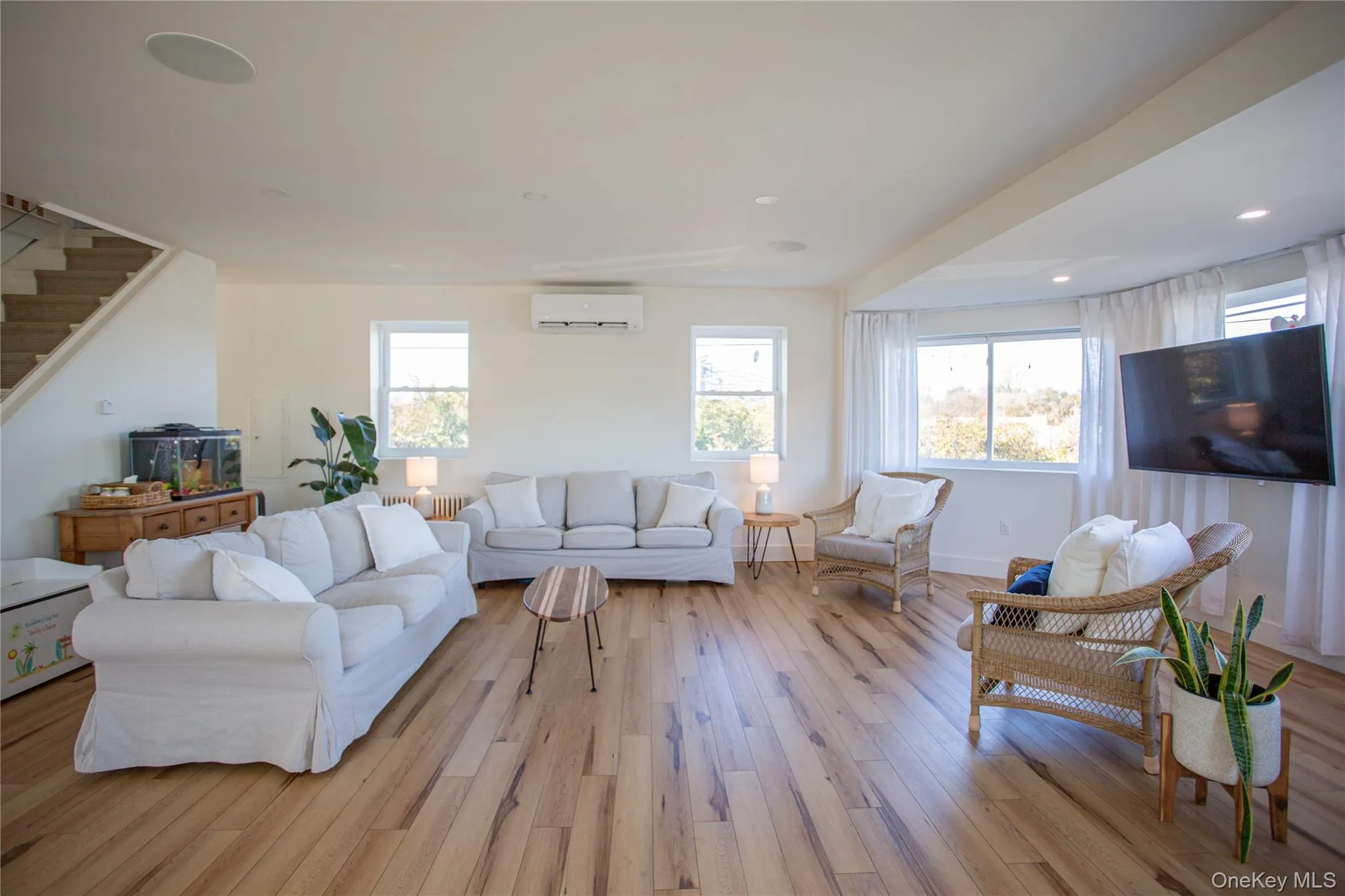 Living area featuring light wood finished floors, healthy amount of natural light, stairs, a wall unit AC, and recessed lighting Living area featuring light wood finished floors, healthy amount of natural light, stairs, a wall unit AC, and recessed lighting