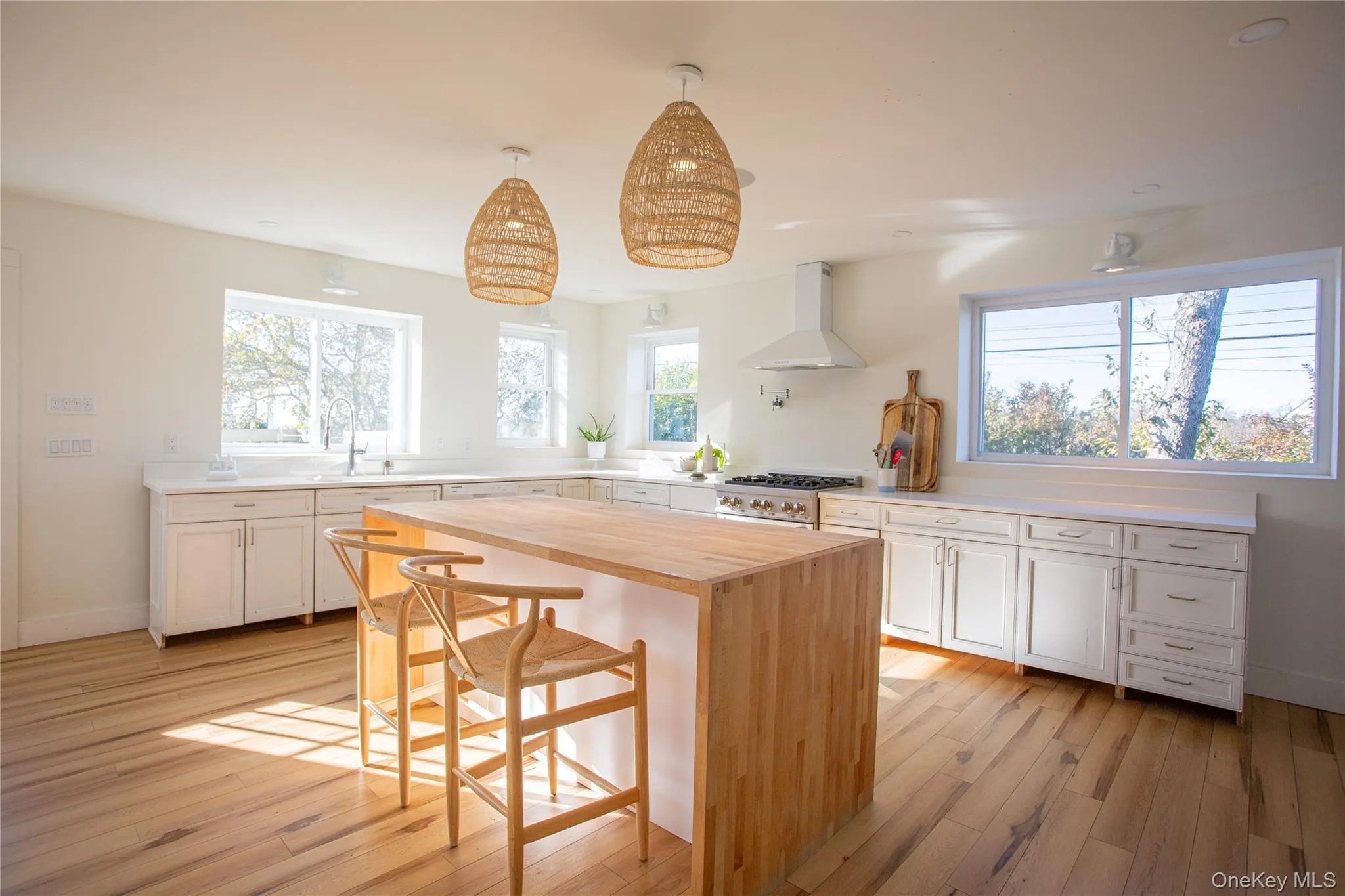 Kitchen with butcher block counters, a kitchen bar, white cabinets, wall chimney exhaust hood, and a center island Kitchen with butcher block counters, a kitchen bar, white cabinets, wall chimney exhaust hood, and a center island