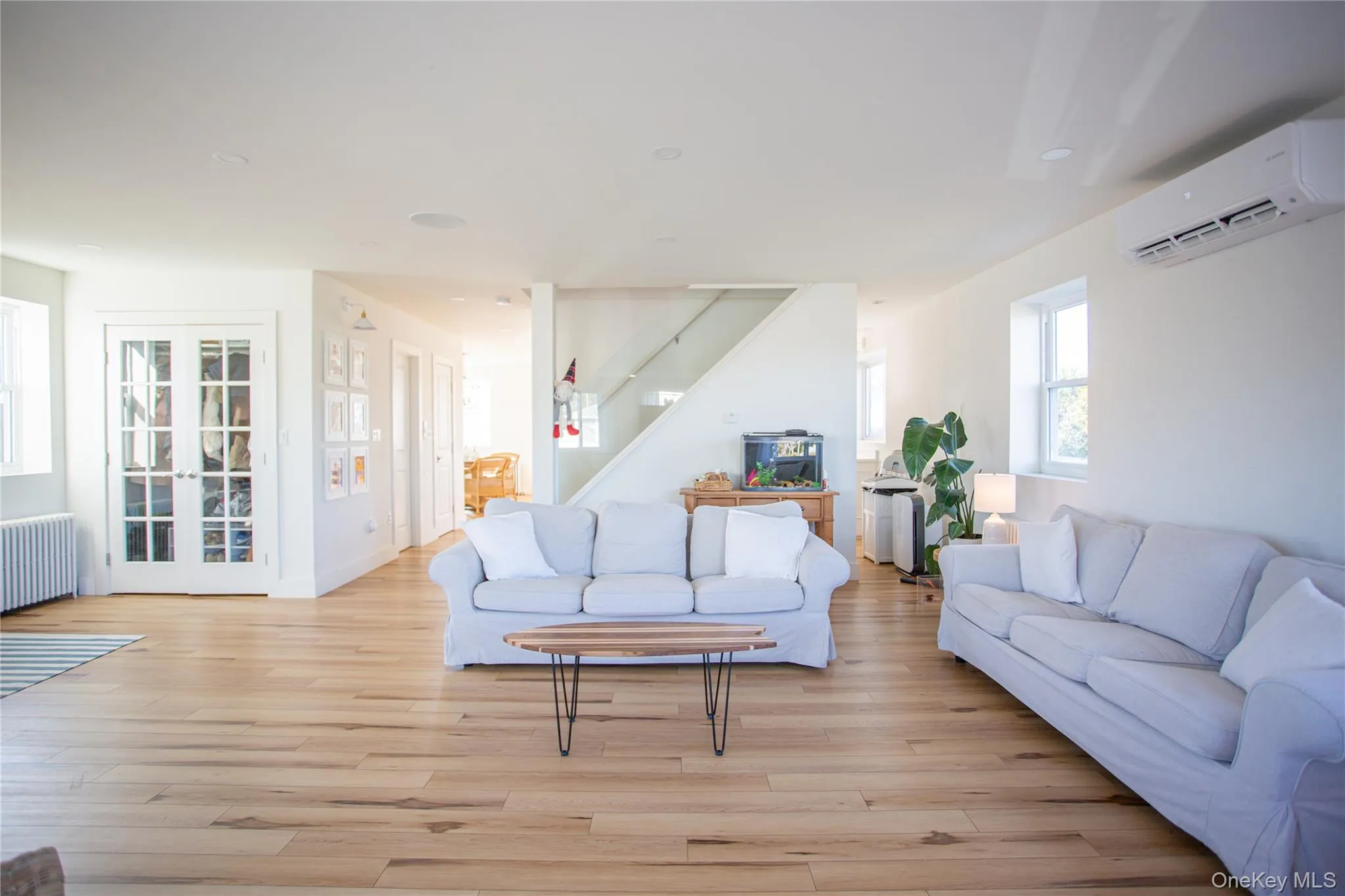 Living area featuring healthy amount of natural light, radiator, stairway, and an AC wall unit Living area featuring healthy amount of natural light, radiator, stairway, and an AC wall unit