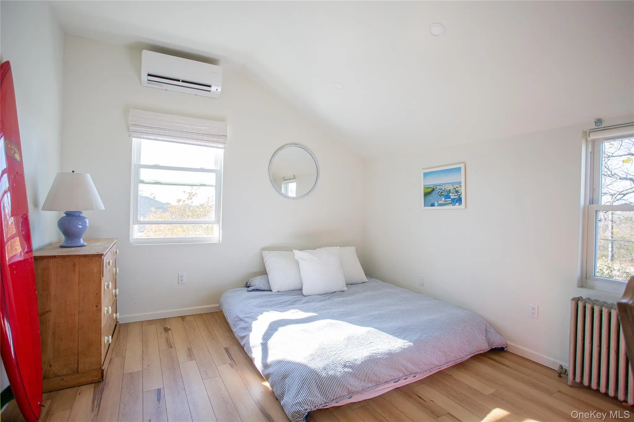Bedroom featuring radiator heating unit, a wall mounted AC, light wood finished floors, and vaulted ceiling Bedroom featuring radiator heating unit, a wall mounted AC, light wood finished floors, and vaulted ceiling