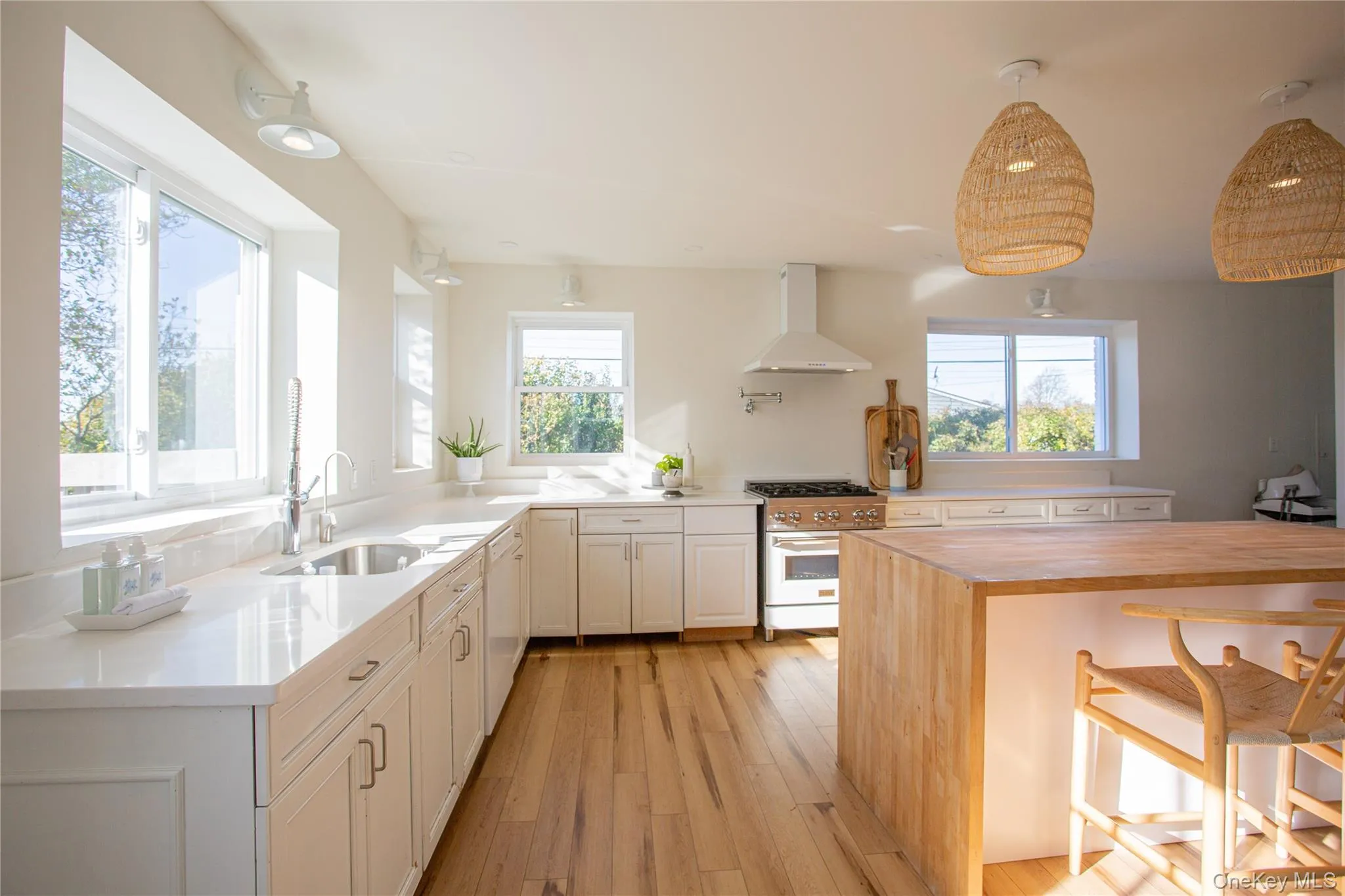 Kitchen with butcher block countertops, a kitchen bar, range with gas stovetop, wall chimney exhaust hood, and white cabinetry Kitchen with butcher block countertops, a kitchen bar, range with gas stovetop, wall chimney exhaust hood, and white cabinetry