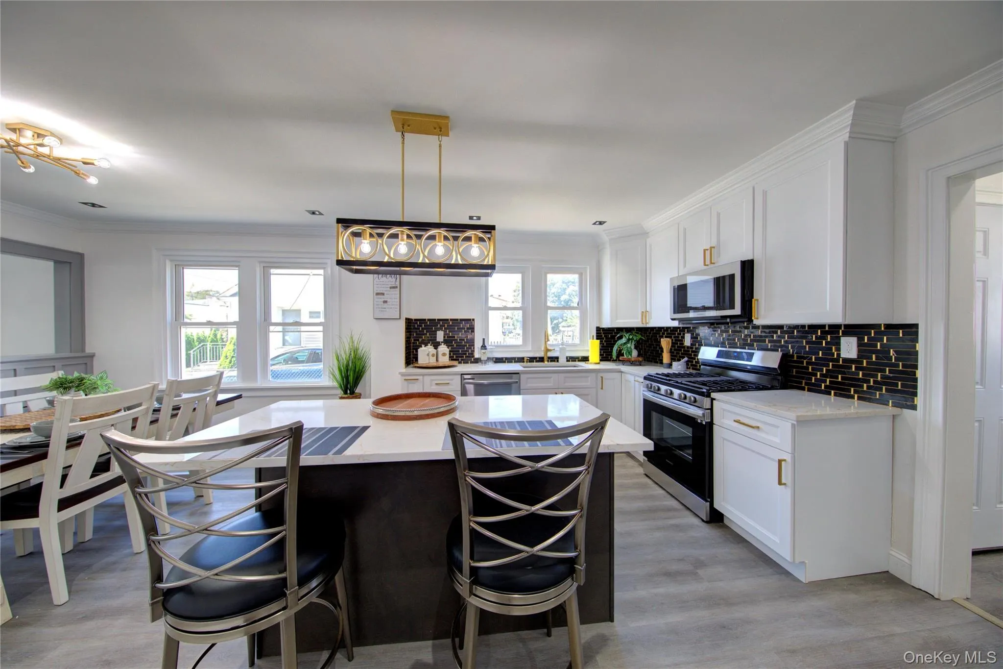 Kitchen with appliances with stainless steel finishes, ornamental molding, white cabinets, decorative light fixtures, and a center island Kitchen with appliances with stainless steel finishes, ornamental molding, white cabinets, decorative light fixtures, and a center island