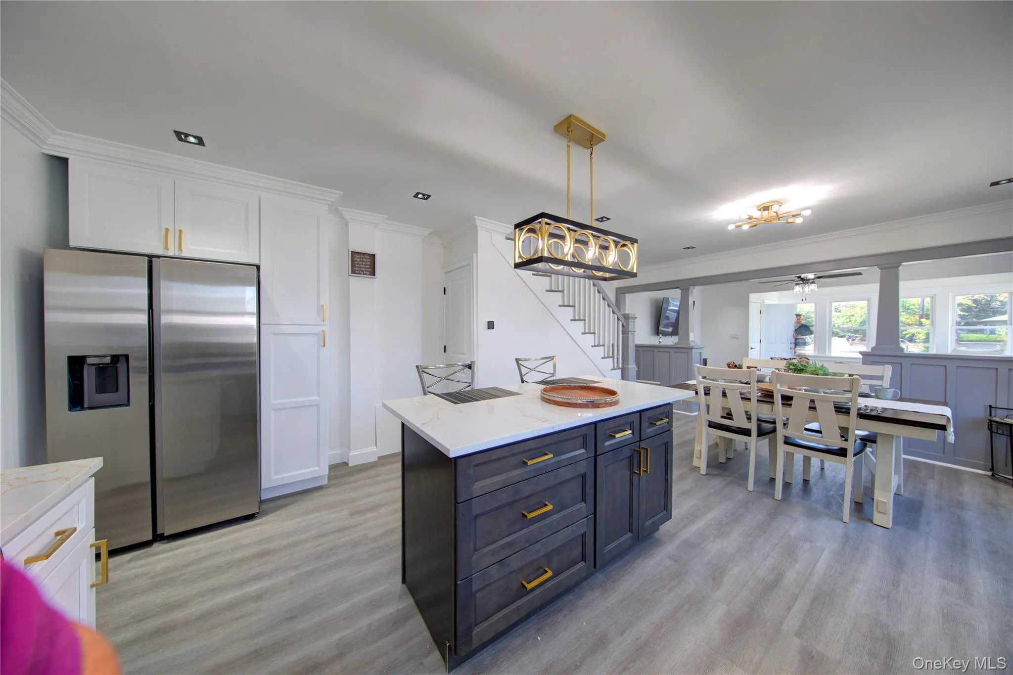 Kitchen with ornamental molding, stainless steel refrigerator with ice dispenser, white cabinets, light stone counters, and decorative light fixtures Kitchen with ornamental molding, stainless steel refrigerator with ice dispenser, white cabinets, light stone counters, and decorative light fixtures