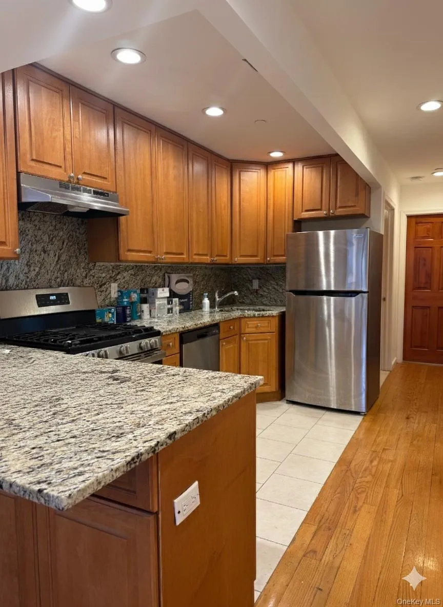 Kitchen featuring brown cabinetry, light stone counters, appliances with stainless steel finishes, tasteful backsplash, and a peninsula Kitchen featuring brown cabinetry, light stone counters, appliances with stainless steel finishes, tasteful backsplash, and a peninsula