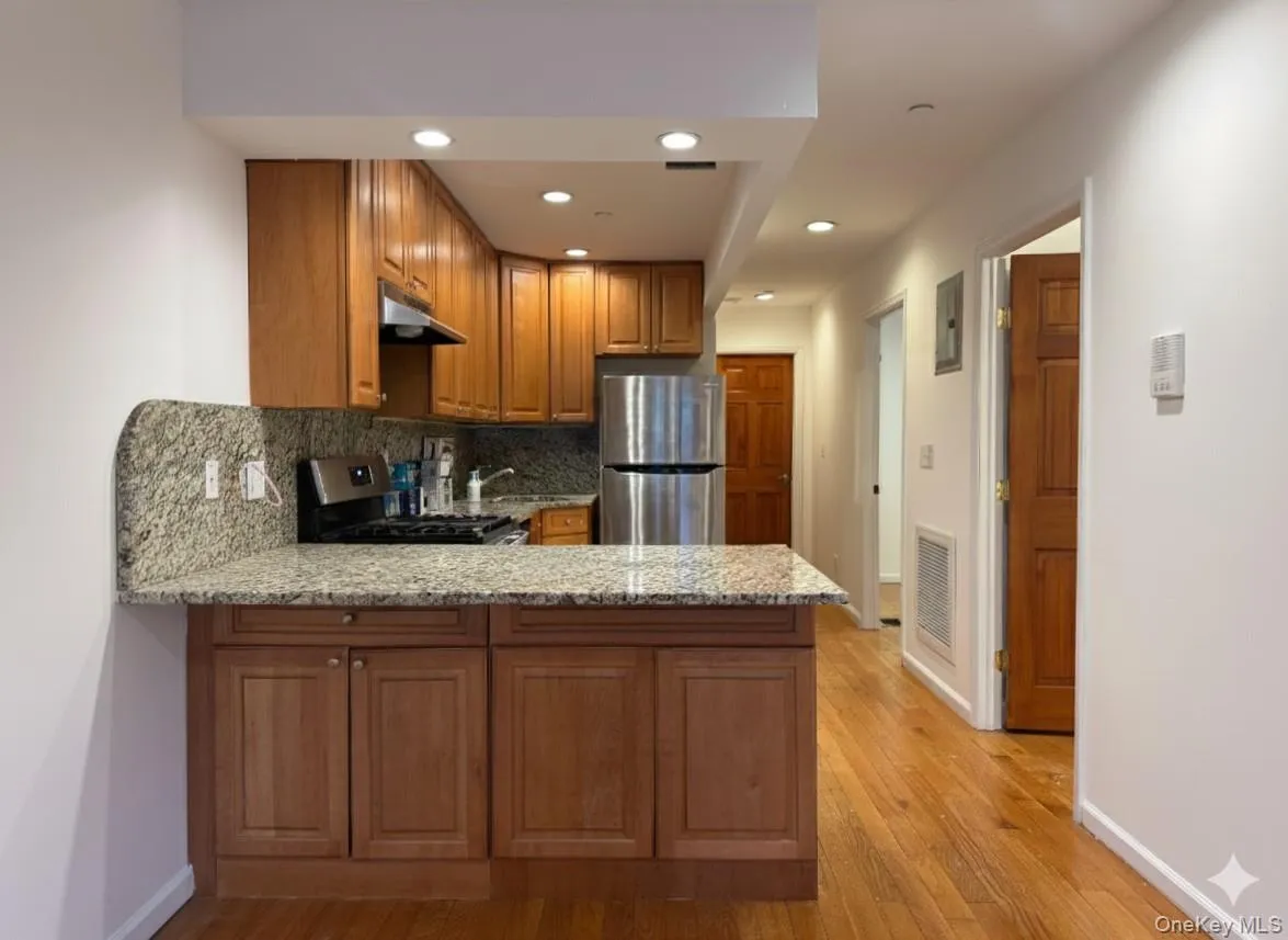 Kitchen featuring brown cabinets, a peninsula, light stone counters, tasteful backsplash, and appliances with stainless steel finishes Kitchen featuring brown cabinets, a peninsula, light stone counters, tasteful backsplash, and appliances with stainless steel finishes