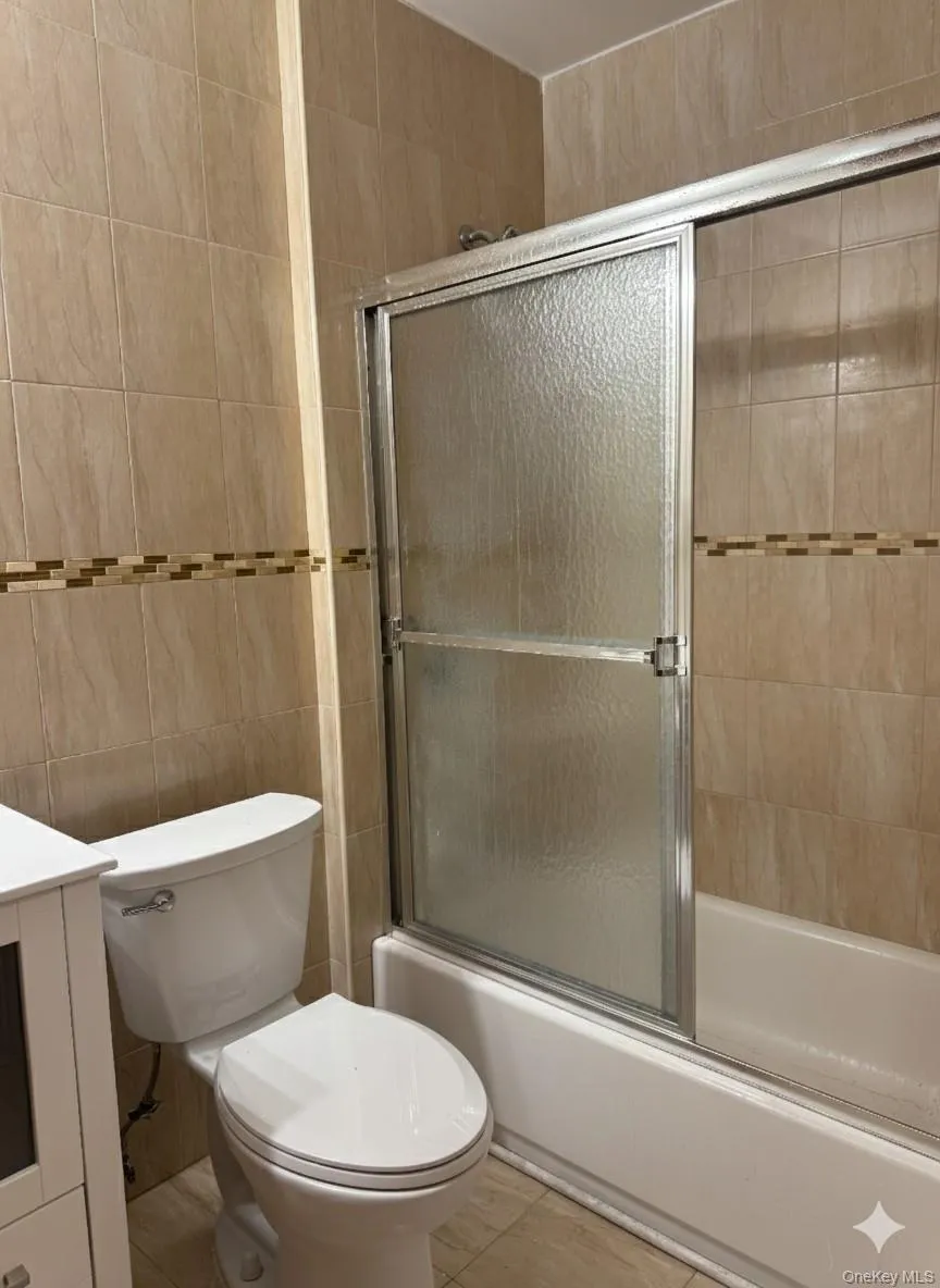 Full bathroom with vanity, shower / bath combination with glass door, and tile walls Full bathroom with vanity, shower / bath combination with glass door, and tile walls