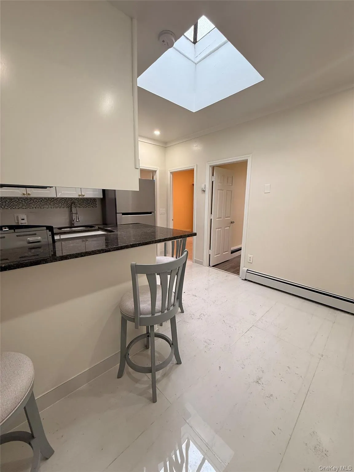 Kitchen featuring a breakfast bar, dark stone counters, baseboard heating, a skylight, and freestanding refrigerator Kitchen featuring a breakfast bar, dark stone counters, baseboard heating, a skylight, and freestanding refrigerator
