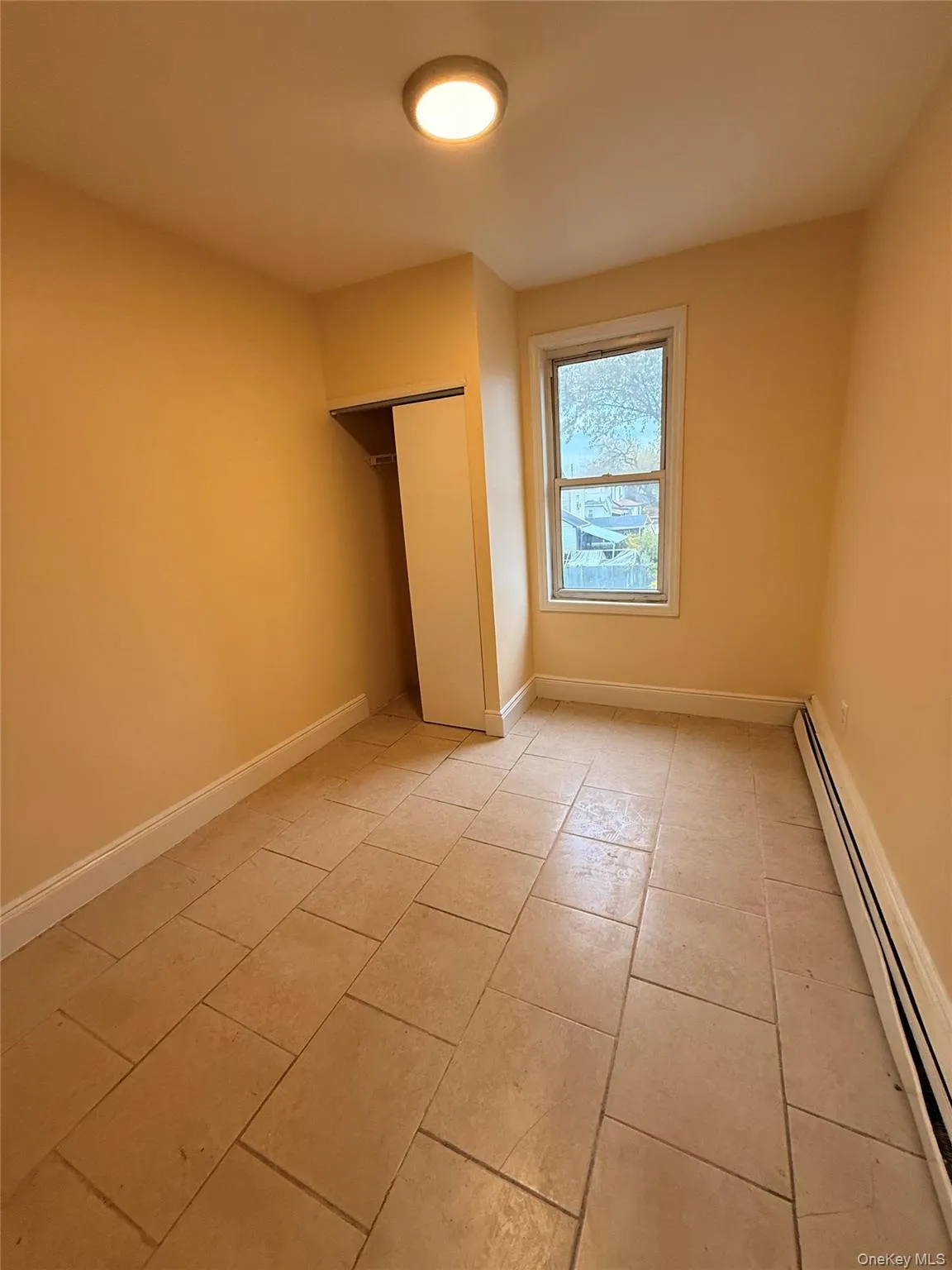 Unfurnished bedroom featuring baseboard heating, a closet, and light tile patterned floors Unfurnished bedroom featuring baseboard heating, a closet, and light tile patterned floors