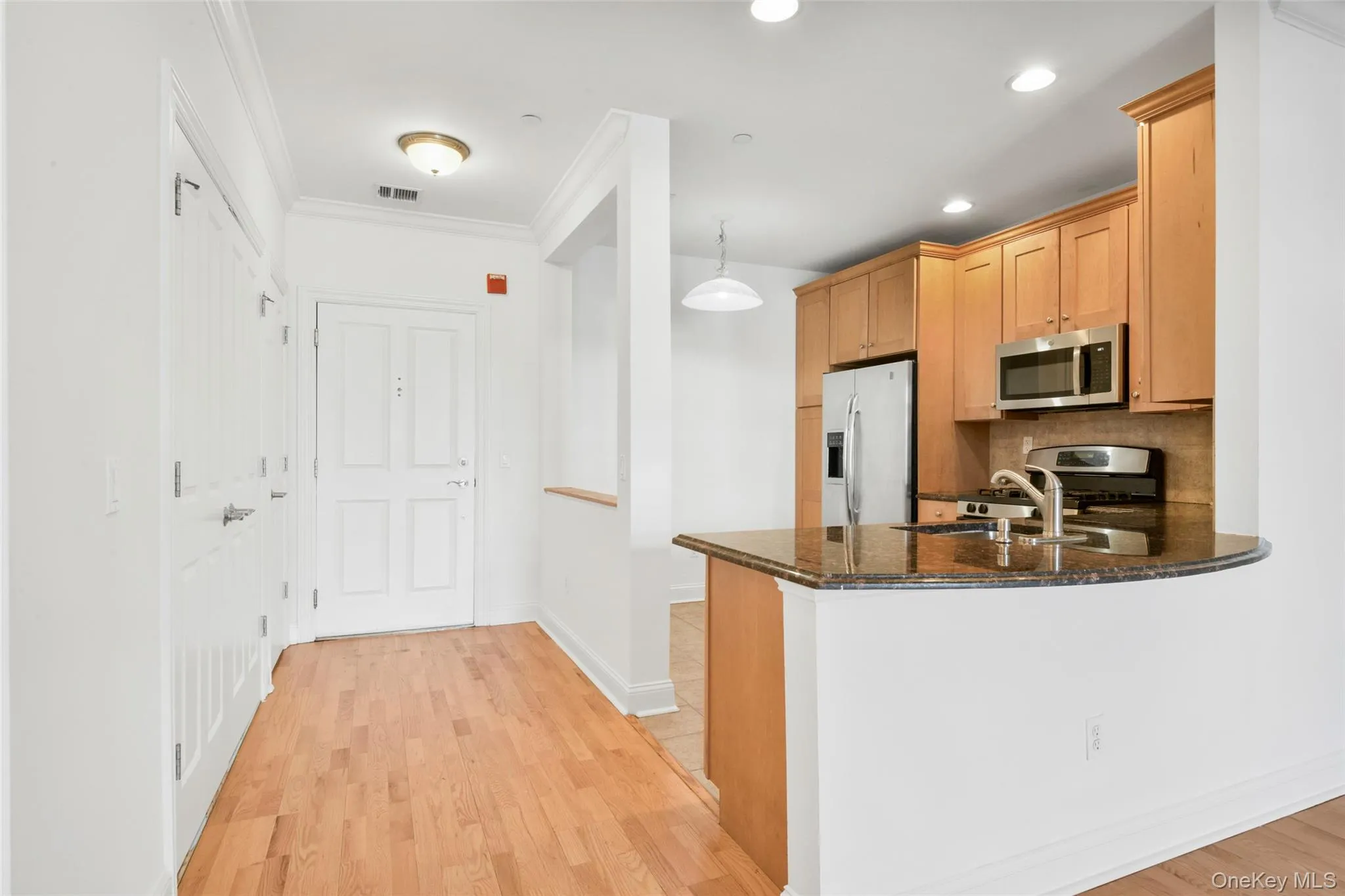Kitchen with dark stone countertops, stainless steel appliances, decorative light fixtures, ornamental molding, and light wood-style floors Kitchen with dark stone countertops, stainless steel appliances, decorative light fixtures, ornamental molding, and light wood-style floors