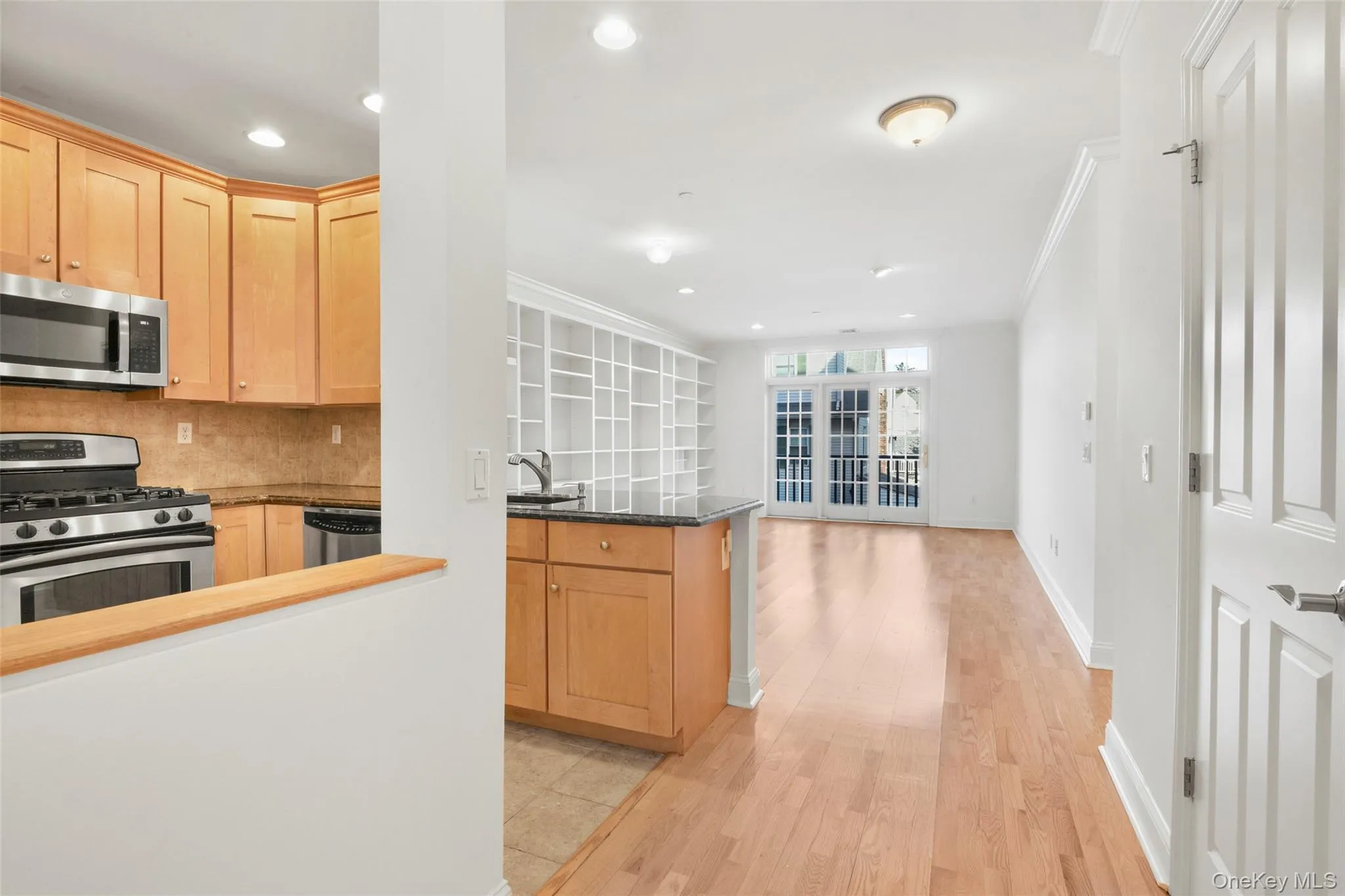 Kitchen with light brown cabinetry, stainless steel appliances, decorative backsplash, dark stone countertops, and ornamental molding Kitchen with light brown cabinetry, stainless steel appliances, decorative backsplash, dark stone countertops, and ornamental molding