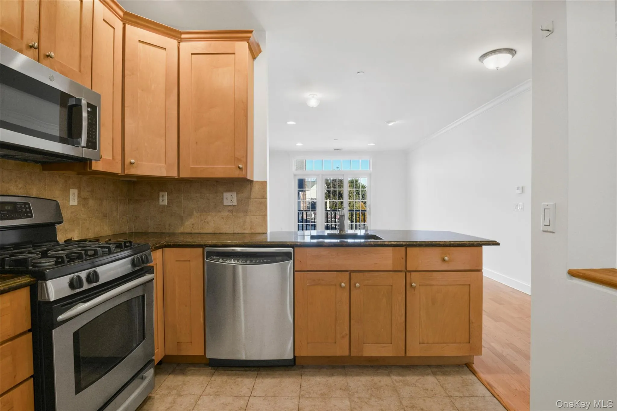 Kitchen with stainless steel appliances, tasteful backsplash, a peninsula, crown molding, and brown cabinetry Kitchen with stainless steel appliances, tasteful backsplash, a peninsula, crown molding, and brown cabinetry