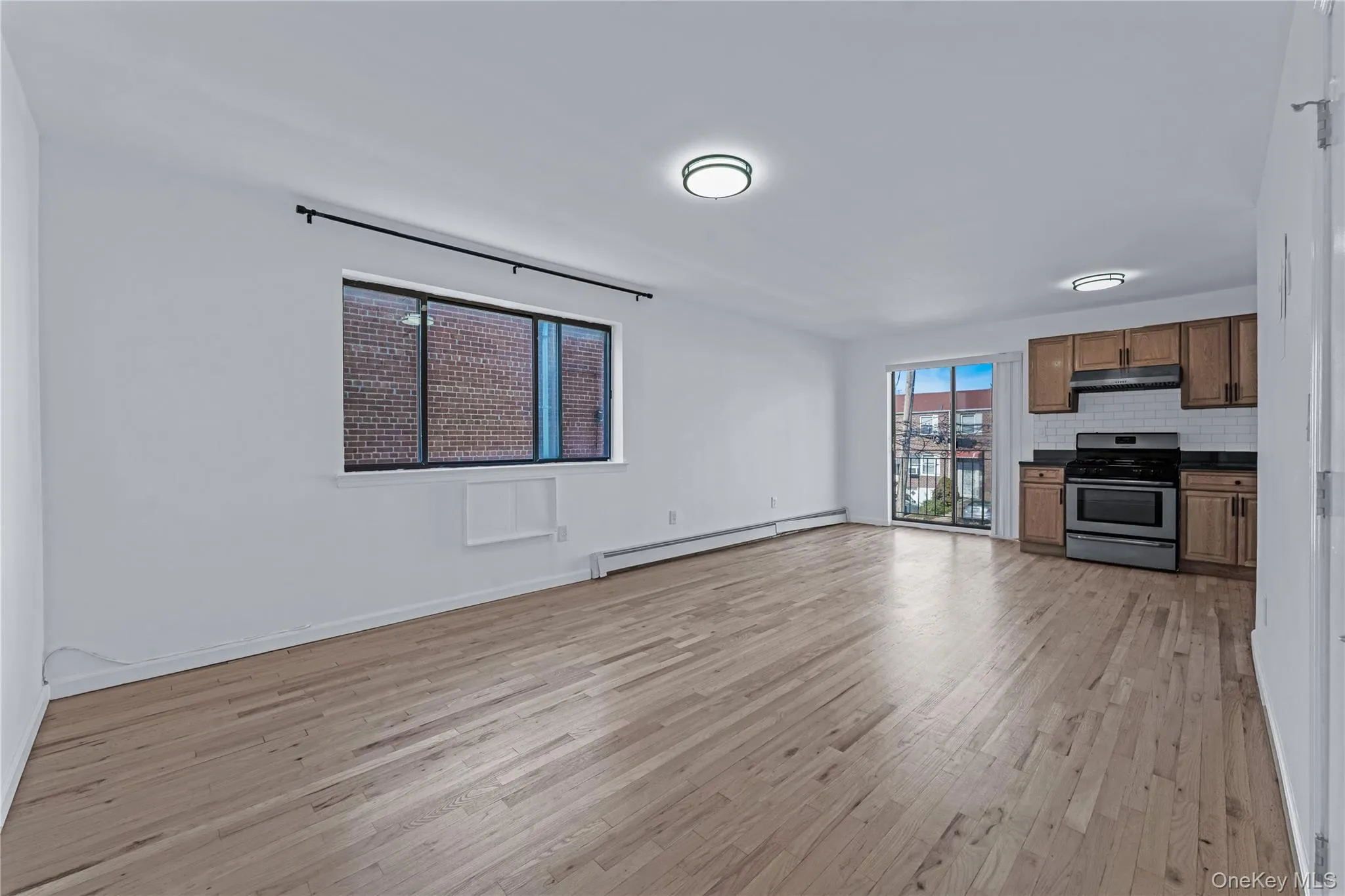 Unfurnished living room featuring light wood-type flooring and baseboard heating Unfurnished living room featuring light wood-type flooring and baseboard heating