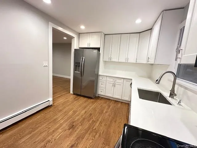 Kitchen with white cabinetry, stainless steel fridge with ice dispenser, recessed lighting, light wood-style floors, and a baseboard radiator Kitchen with white cabinetry, stainless steel fridge with ice dispenser, recessed lighting, light wood-style floors, and a baseboard radiator