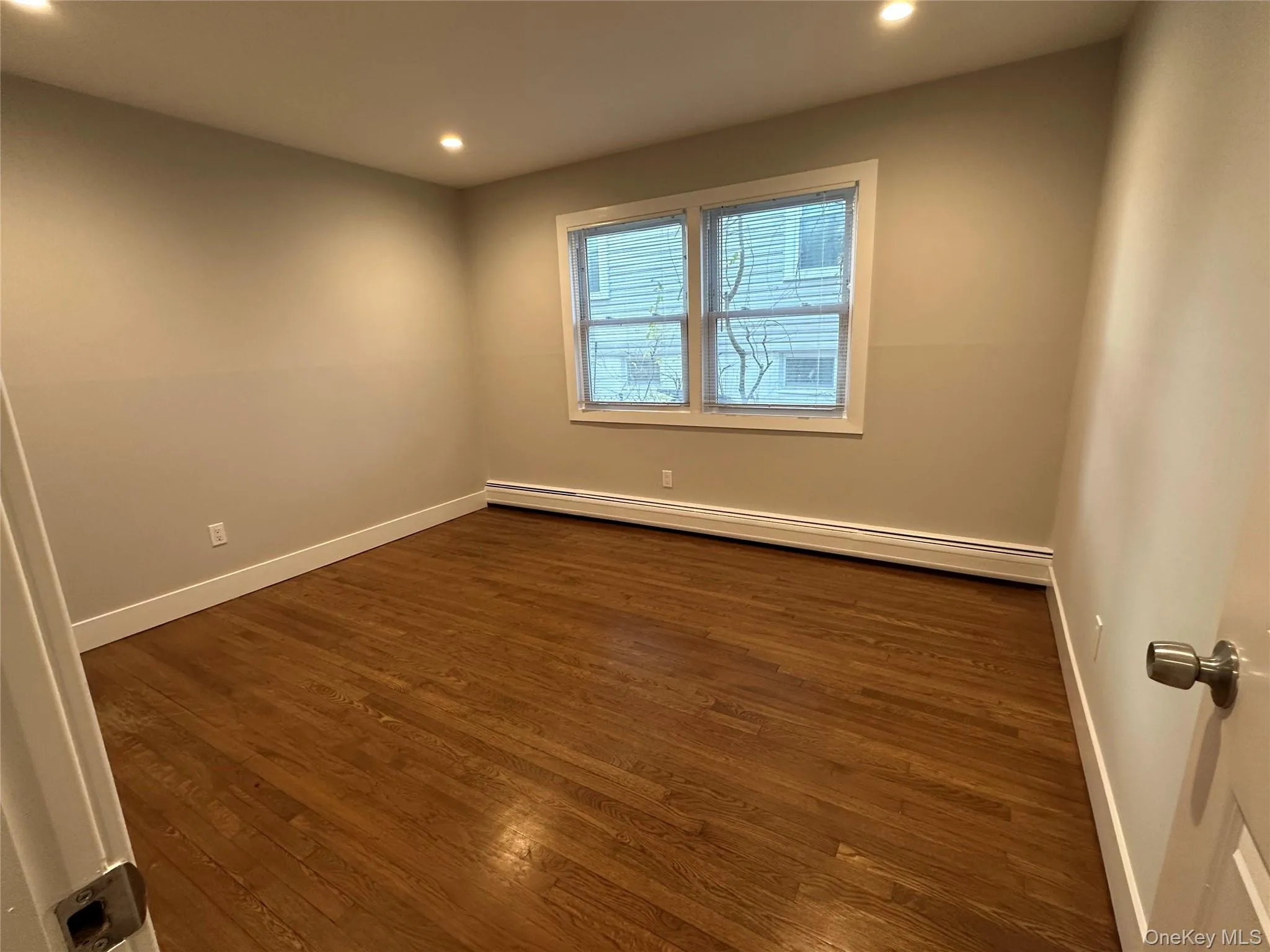 Empty room featuring dark wood finished floors, a baseboard radiator, and recessed lighting Empty room featuring dark wood finished floors, a baseboard radiator, and recessed lighting