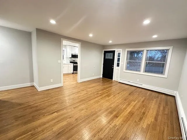 Unfurnished living room with recessed lighting, light wood finished floors, and a baseboard heating unit Unfurnished living room with recessed lighting, light wood finished floors, and a baseboard heating unit