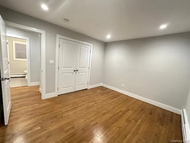 Unfurnished bedroom featuring wood-type flooring, baseboard heating, a closet, recessed lighting, and a baseboard radiator Unfurnished bedroom featuring wood-type flooring, baseboard heating, a closet, recessed lighting, and a baseboard radiator