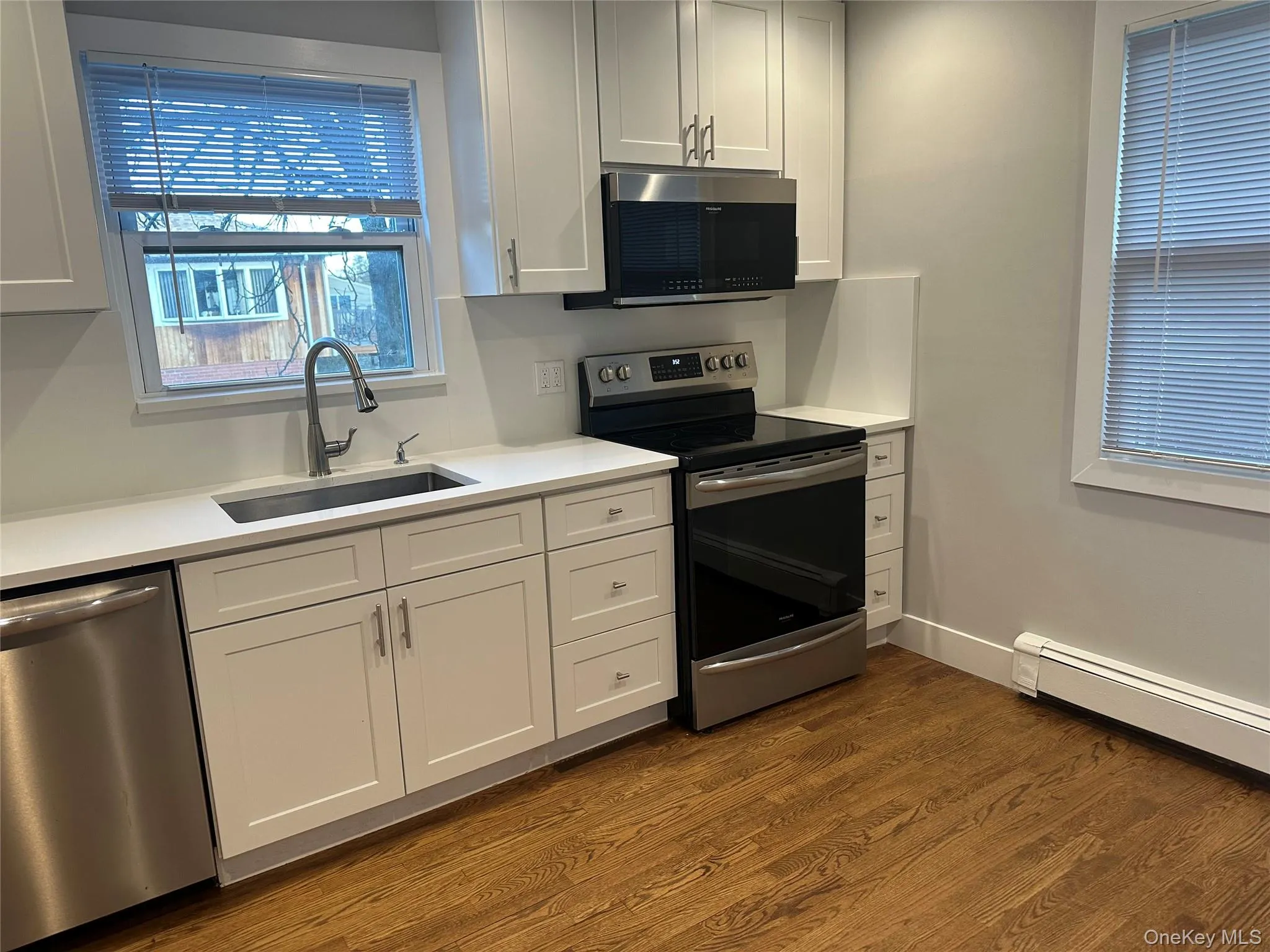 Kitchen featuring appliances with stainless steel finishes, white cabinetry, dark wood-type flooring, and light stone countertops Kitchen featuring appliances with stainless steel finishes, white cabinetry, dark wood-type flooring, and light stone countertops
