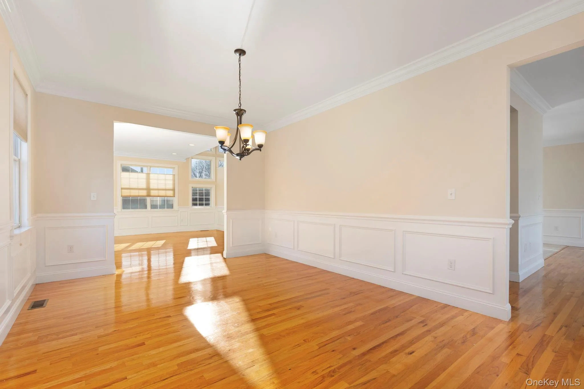 Unfurnished dining area featuring light wood-style flooring, a chandelier, ornamental molding, wainscoting, and a decorative wall Unfurnished dining area featuring light wood-style flooring, a chandelier, ornamental molding, wainscoting, and a decorative wall