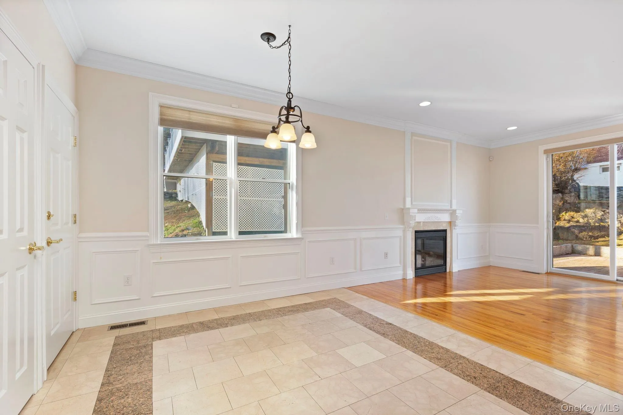 Entrance foyer featuring inlaid floor details, ornamental molding, a chandelier, a wainscoted wall, and a glass covered fireplace Entrance foyer featuring inlaid floor details, ornamental molding, a chandelier, a wainscoted wall, and a glass covered fireplace