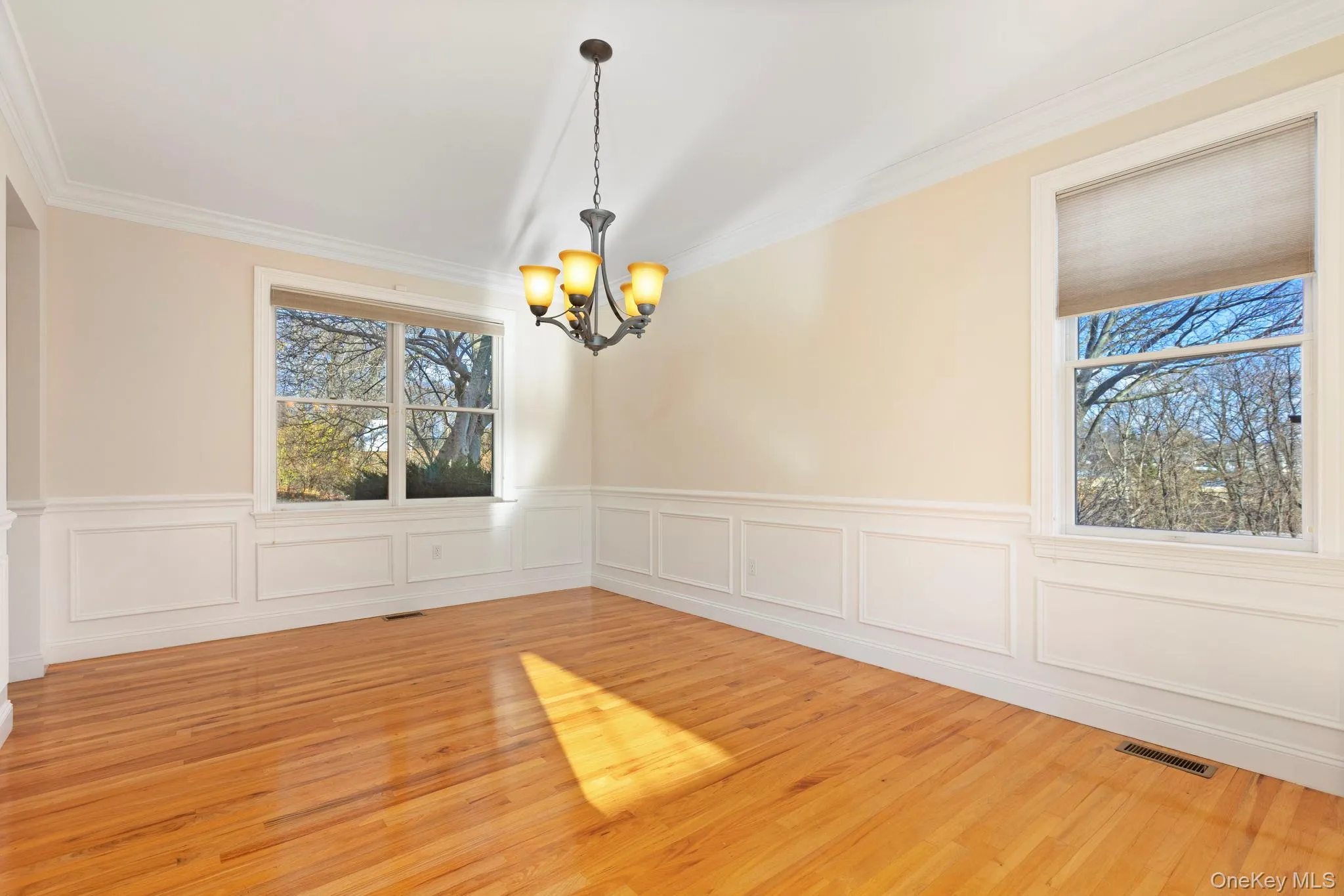 Spare room with a chandelier, wood finished floors, crown molding, and wainscoting Spare room with a chandelier, wood finished floors, crown molding, and wainscoting