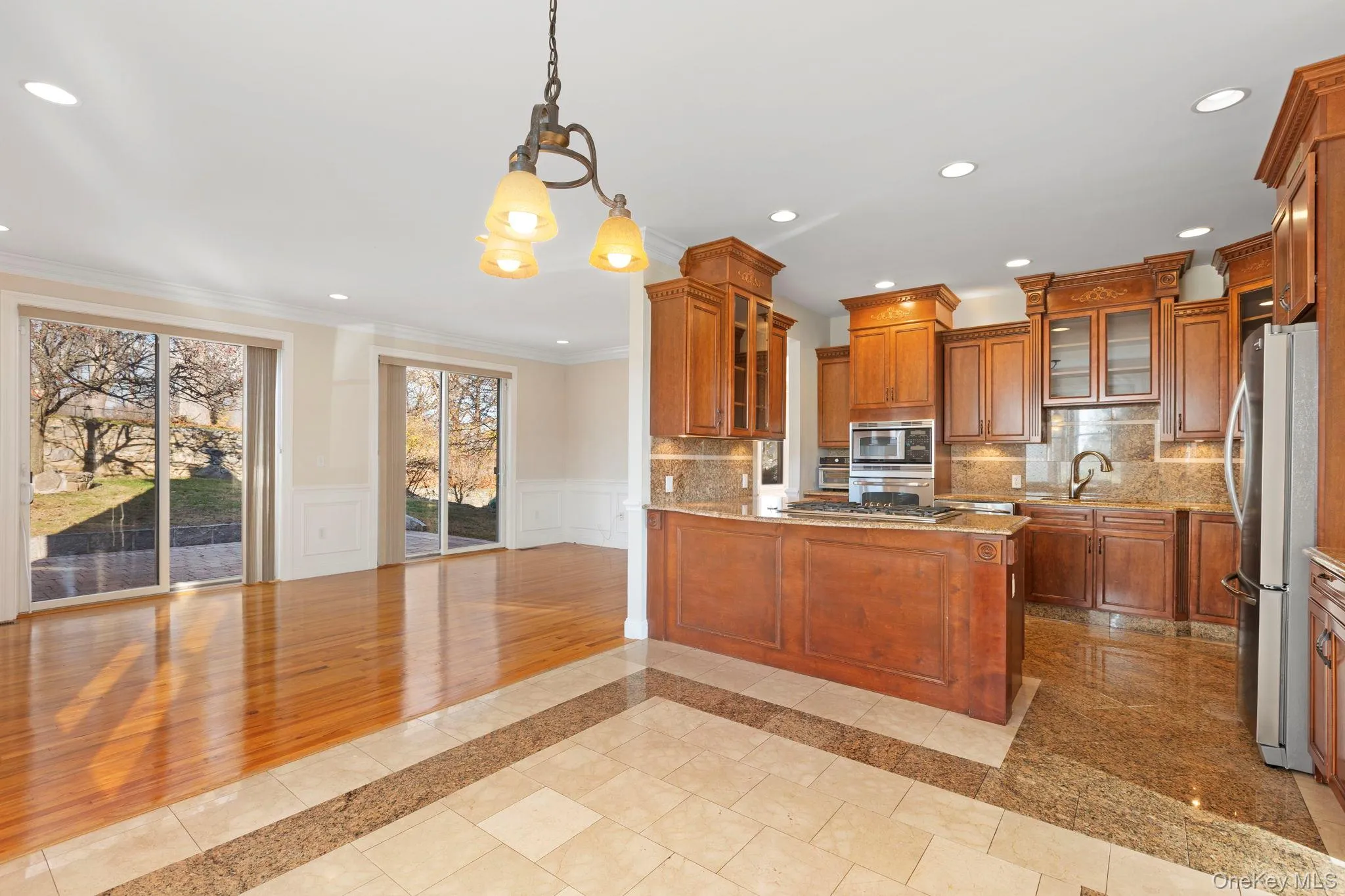 Kitchen featuring inlaid floor details, glass insert cabinets, brown cabinets, hanging light fixtures, and ornamental molding Kitchen featuring inlaid floor details, glass insert cabinets, brown cabinets, hanging light fixtures, and ornamental molding