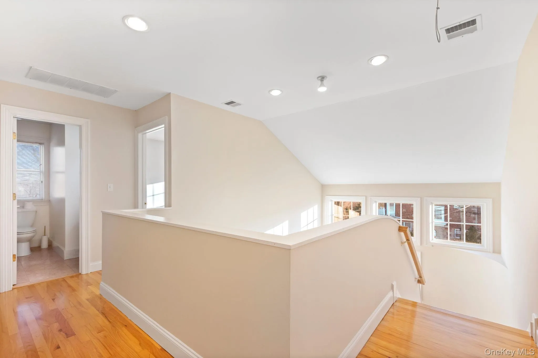 Corridor with an upstairs landing, healthy amount of natural light, recessed lighting, light wood-style floors, and vaulted ceiling Corridor with an upstairs landing, healthy amount of natural light, recessed lighting, light wood-style floors, and vaulted ceiling