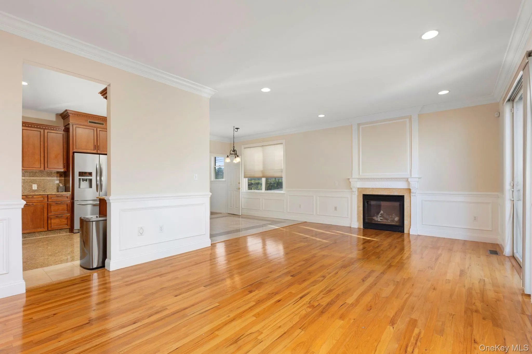 Unfurnished living room featuring light wood finished floors, a glass covered fireplace, ornamental molding, recessed lighting, and a decorative wall Unfurnished living room featuring light wood finished floors, a glass covered fireplace, ornamental molding, recessed lighting, and a decorative wall