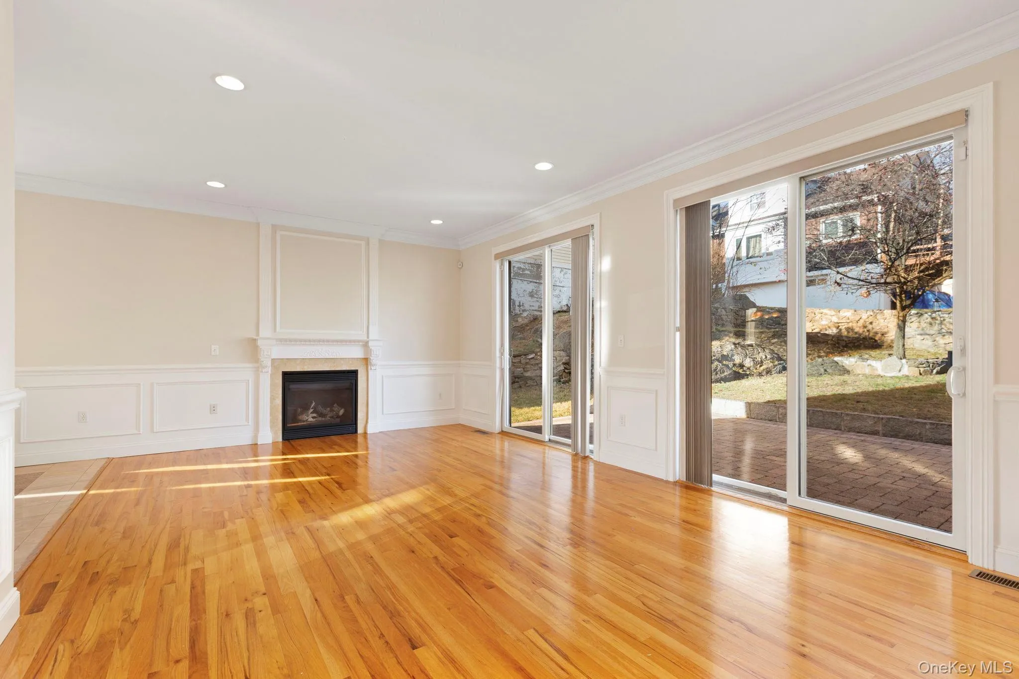 Unfurnished living room with hardwood / wood-style floors, a fireplace, ornamental molding, wainscoting, and a decorative wall Unfurnished living room with hardwood / wood-style floors, a fireplace, ornamental molding, wainscoting, and a decorative wall