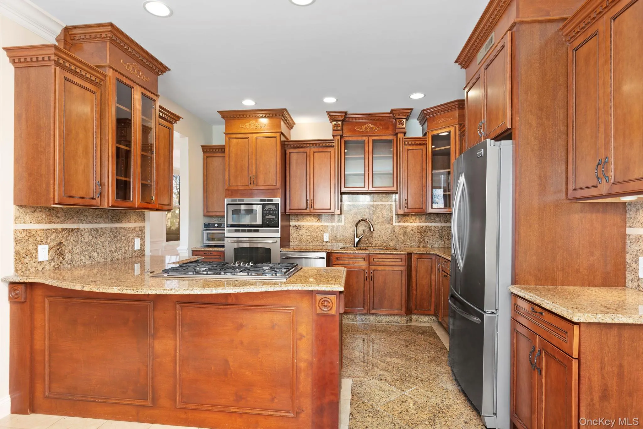 Kitchen featuring granite tiled floors, glass insert cabinets, brown cabinetry, light stone counters, and recessed lighting Kitchen featuring granite tiled floors, glass insert cabinets, brown cabinetry, light stone counters, and recessed lighting
