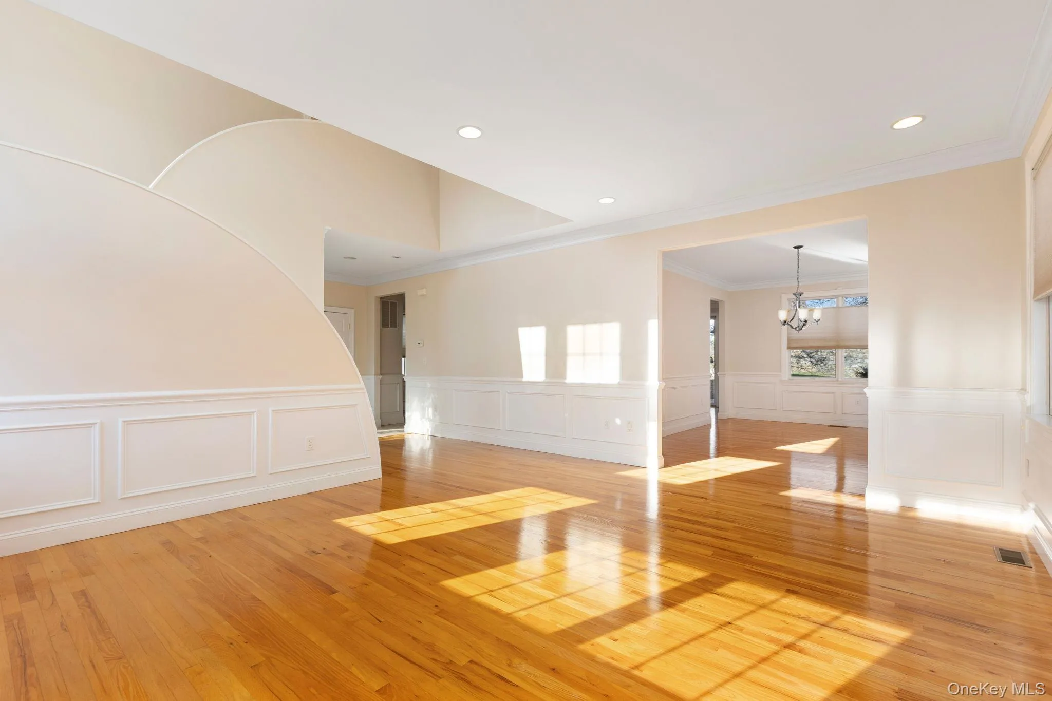 Unfurnished living room featuring light wood-style flooring, wainscoting, a chandelier, ornamental molding, and a decorative wall Unfurnished living room featuring light wood-style flooring, wainscoting, a chandelier, ornamental molding, and a decorative wall