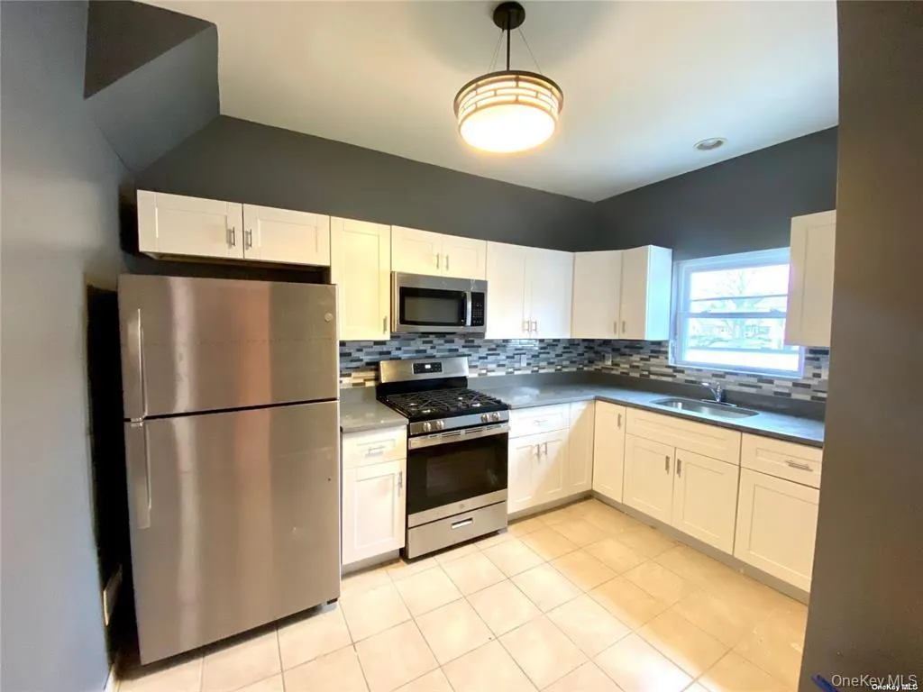 Kitchen featuring appliances with stainless steel finishes, white cabinetry, decorative light fixtures, light tile patterned flooring, and dark countertops Kitchen featuring appliances with stainless steel finishes, white cabinetry, decorative light fixtures, light tile patterned flooring, and dark countertops