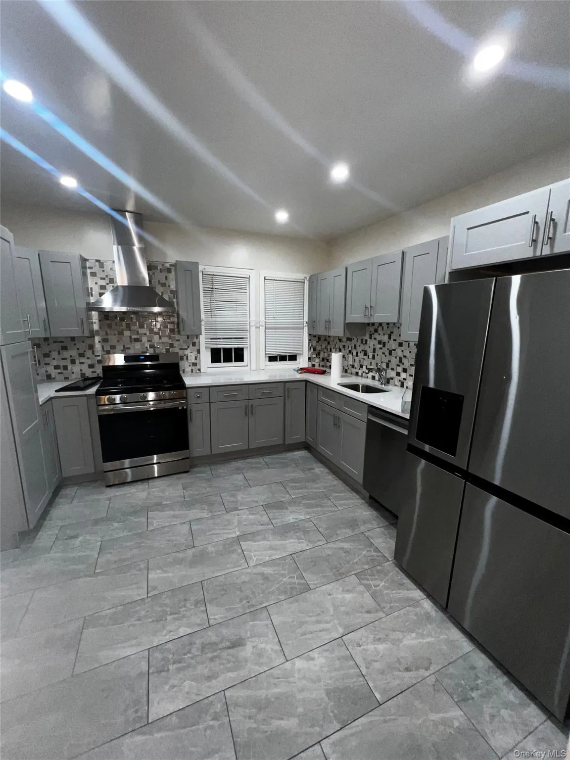 Kitchen featuring stainless steel appliances, gray cabinets, wall chimney exhaust hood, backsplash, and recessed lighting Kitchen featuring stainless steel appliances, gray cabinets, wall chimney exhaust hood, backsplash, and recessed lighting