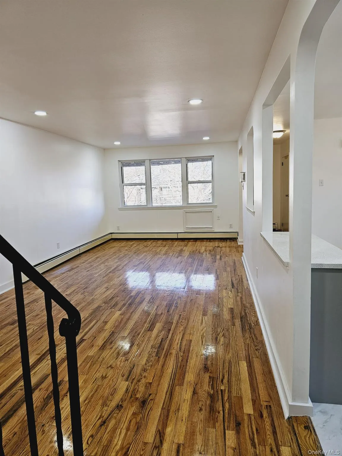Unfurnished room with wood finished floors, arched walkways, baseboard heating, and recessed lighting Unfurnished room with wood finished floors, arched walkways, baseboard heating, and recessed lighting
